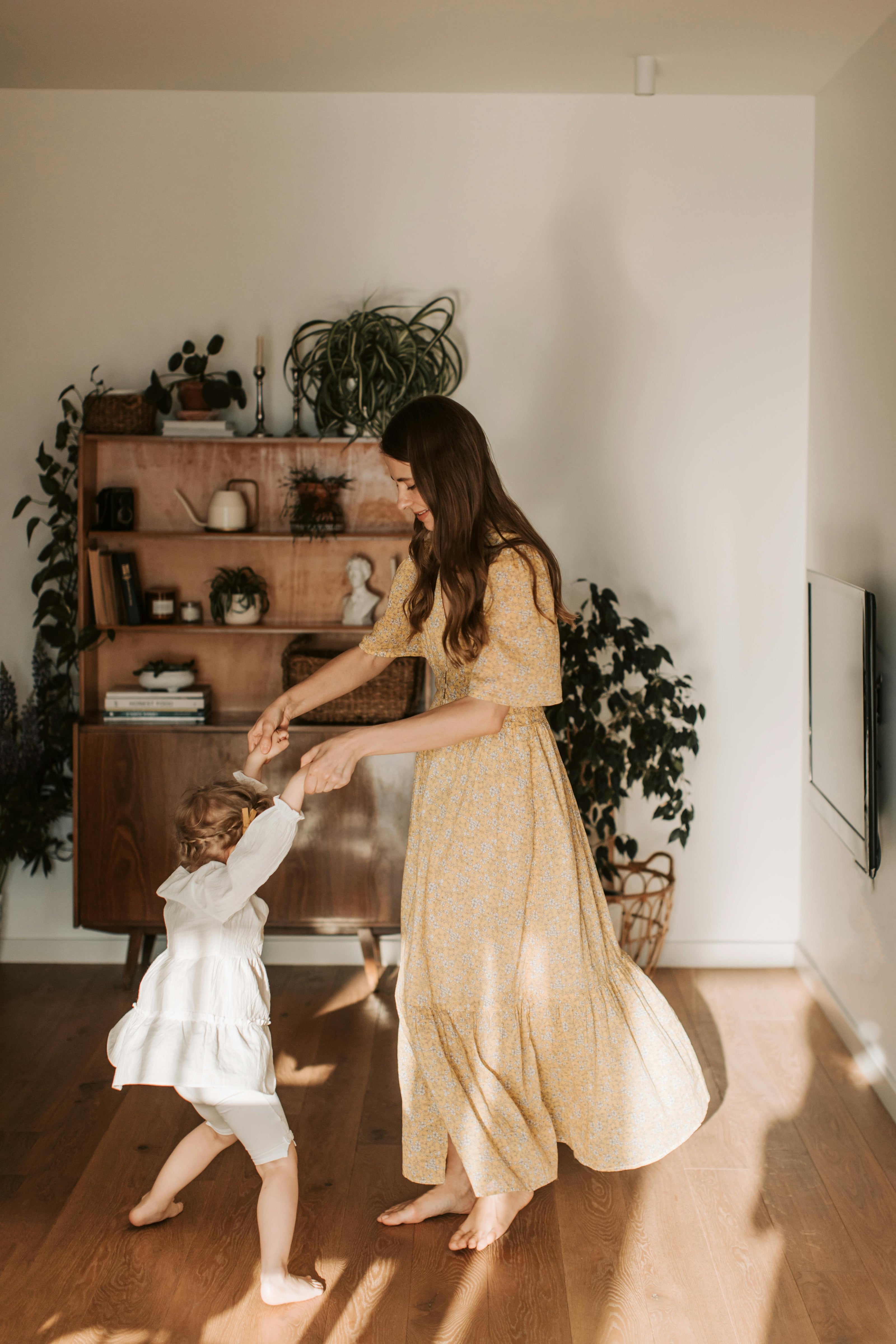 mother and young daughter dancing together in a living space with mid century furniture and plants on a natural vintage looking hard wood floor