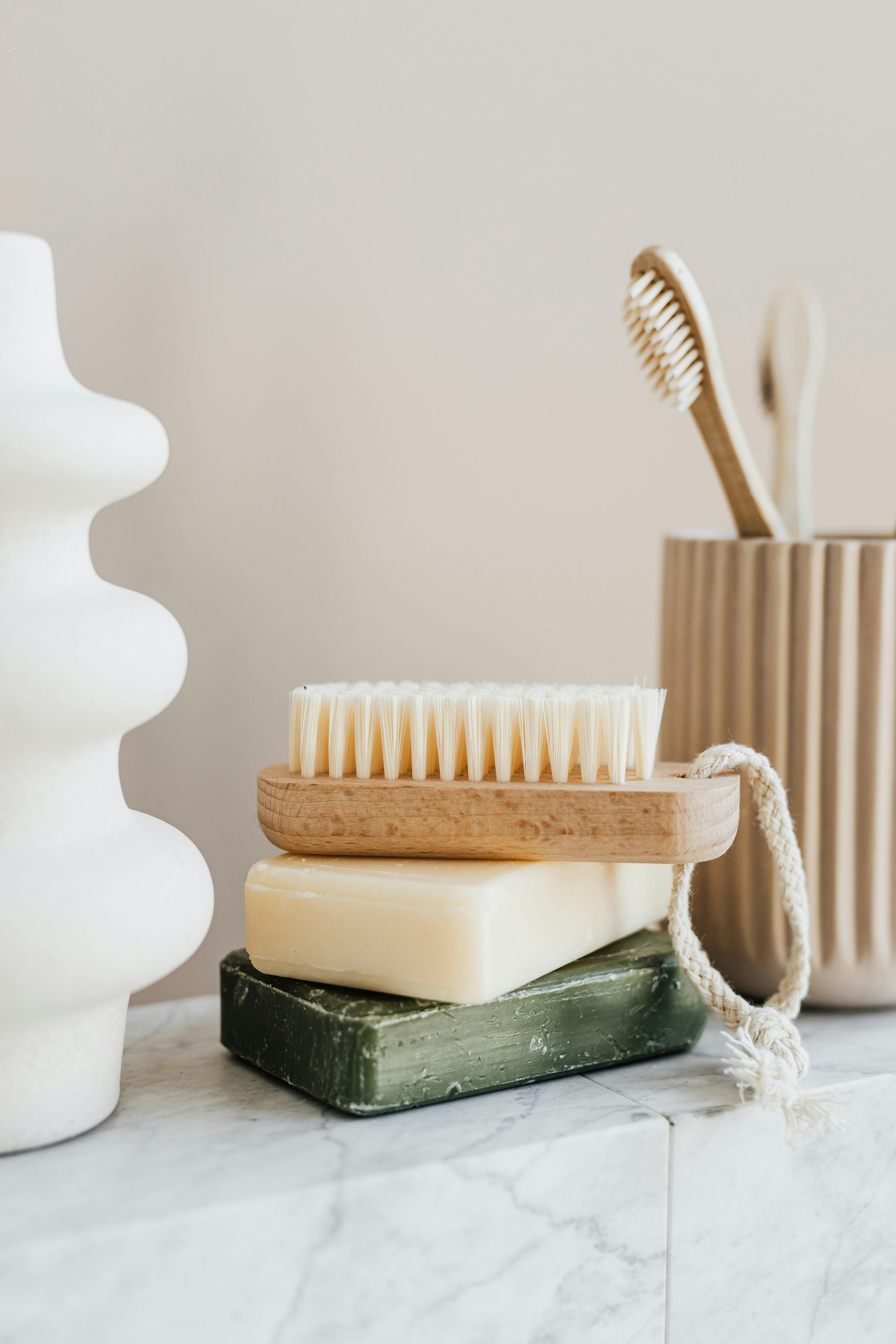 Natural-soaps-with-nail-scrub-and-wooden-tooth-brushes-next-to-a-white-modern-vase-on-a-marble-bathroom-counter