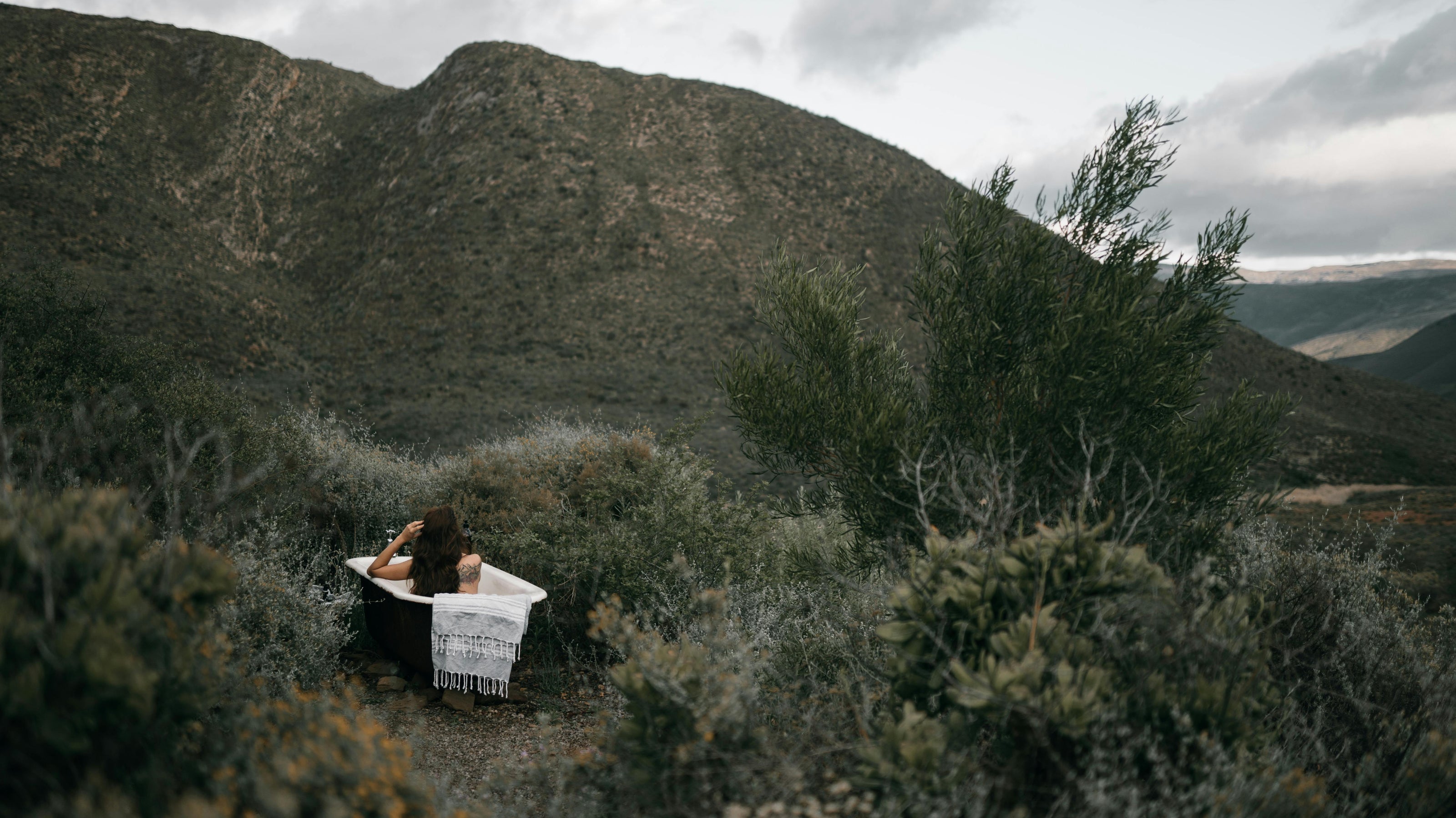 photo of a woman sitting in an outdoor bath tub with beautiful long hair looking out into the nature in front of her