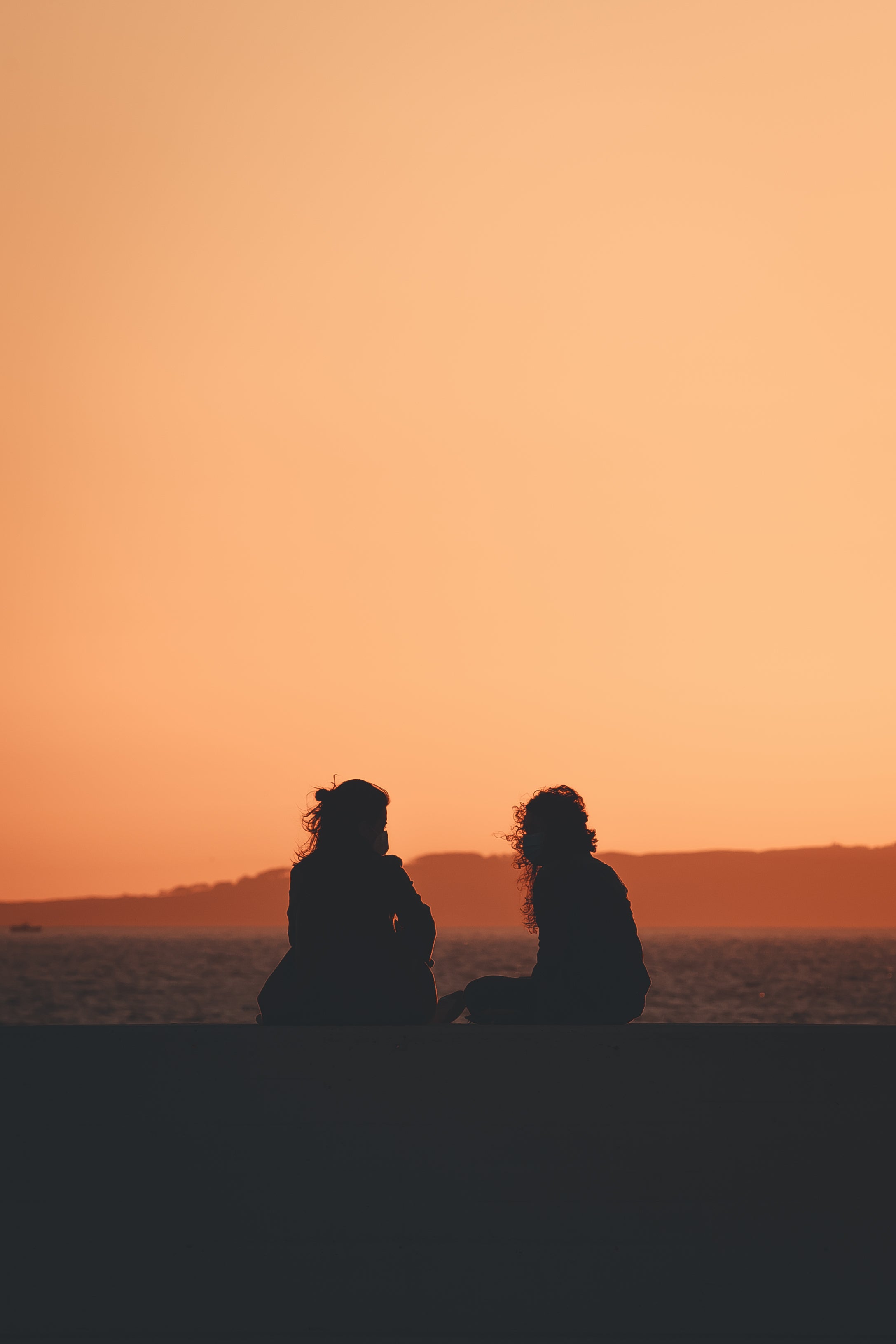 two women sitting in nature silhouetted by the settings sun