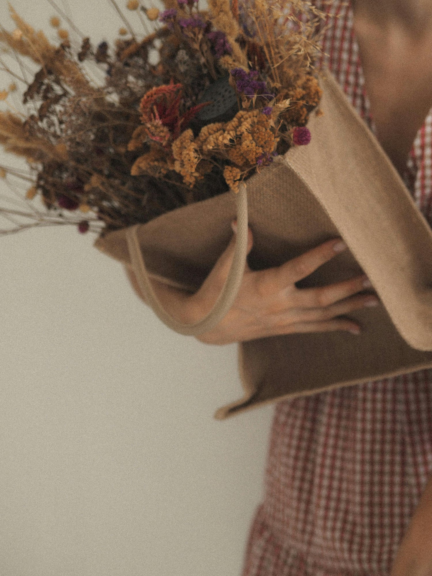 A woman wearing a cute checkered dress holding a brown bag full of dried flowers